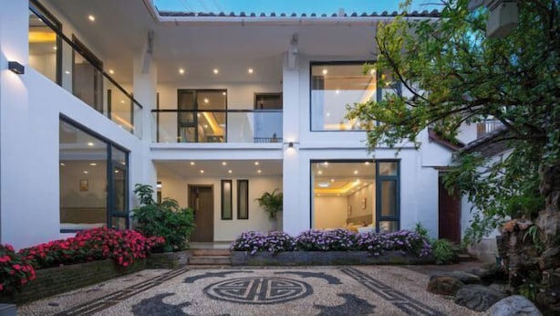 Um edifício moderno de dois andares com entrada central, janelas amplas e um jardim bem cuidado com flores e pedras.