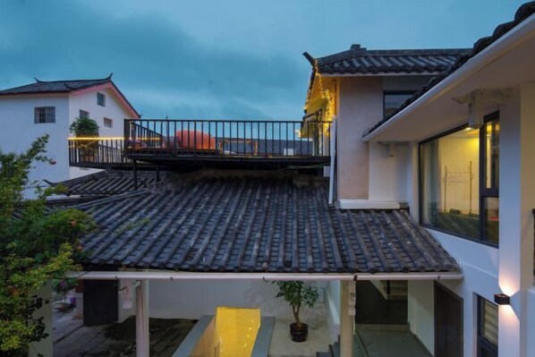 A residential building with a tiled roof, a balcony with a railing, and a small garden area with potted plants. - Xinniu Inn (Lijiang Ancient City Dashuiche Shop) (Lijiang)