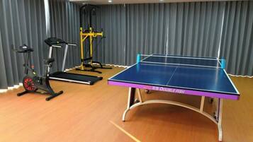 Une pièce équipée d’une table de ping-pong, de vélos d’exercice et d’un appareil de musculation jaune.