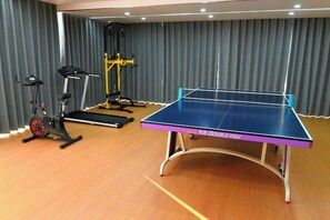Een kamer met een tafeltennistafel, een paar trainingsfietsen en een geel fitnessapparaat.