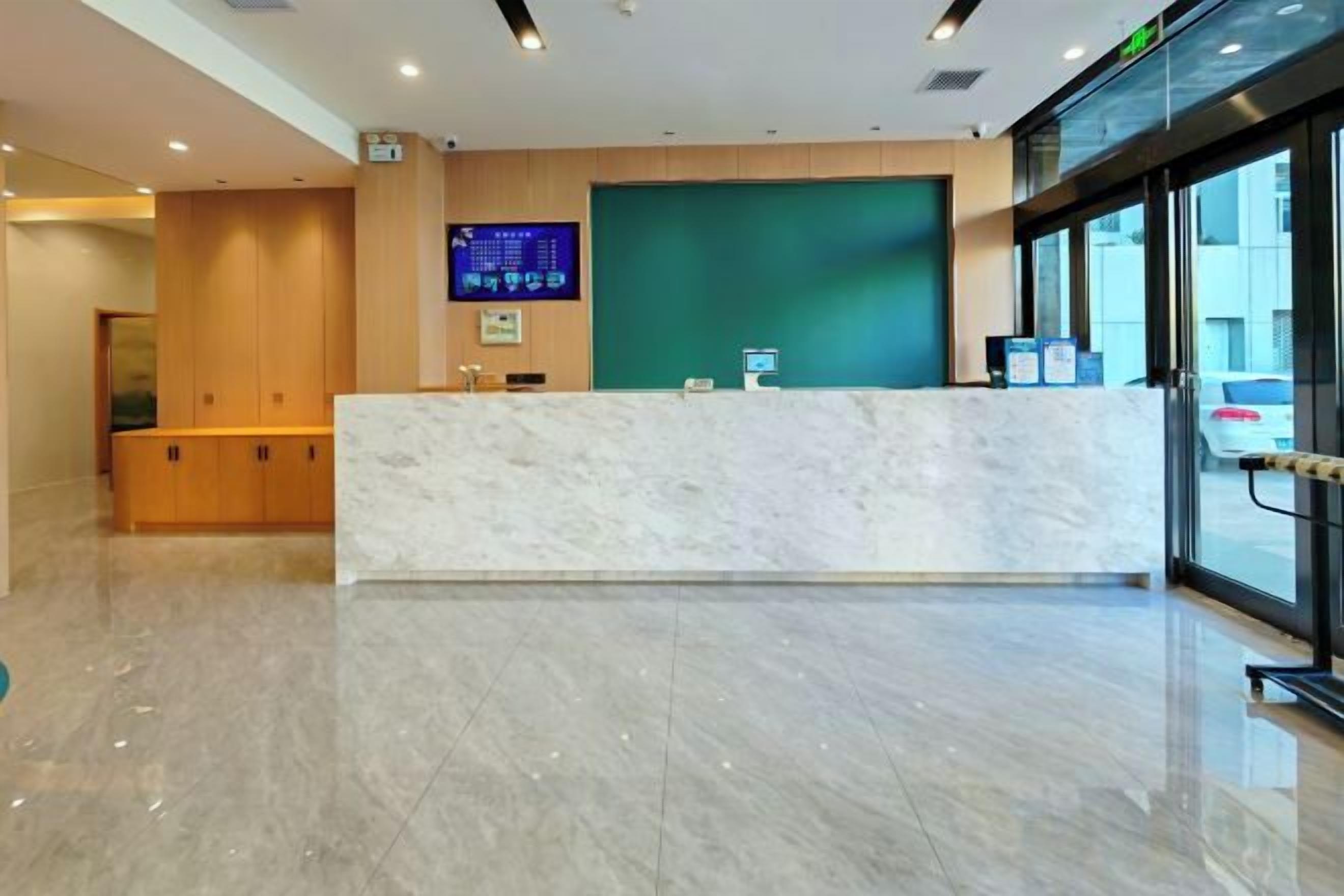 A hotel reception area with a marble counter, a digital display, and a green wall.