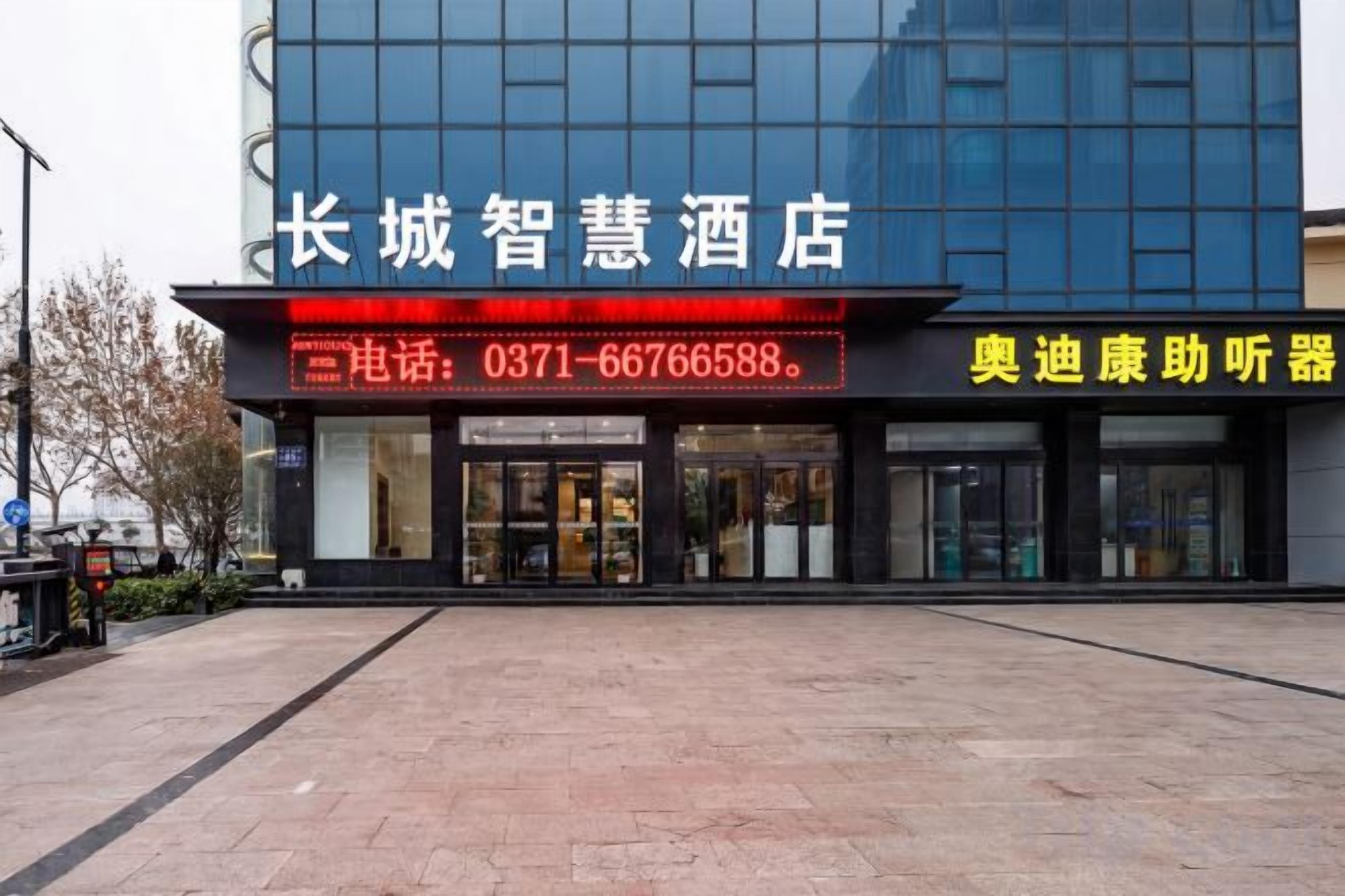 A modern hotel with a glass facade, a prominent entrance with a red sign, and a clear pathway leading to the entrance.