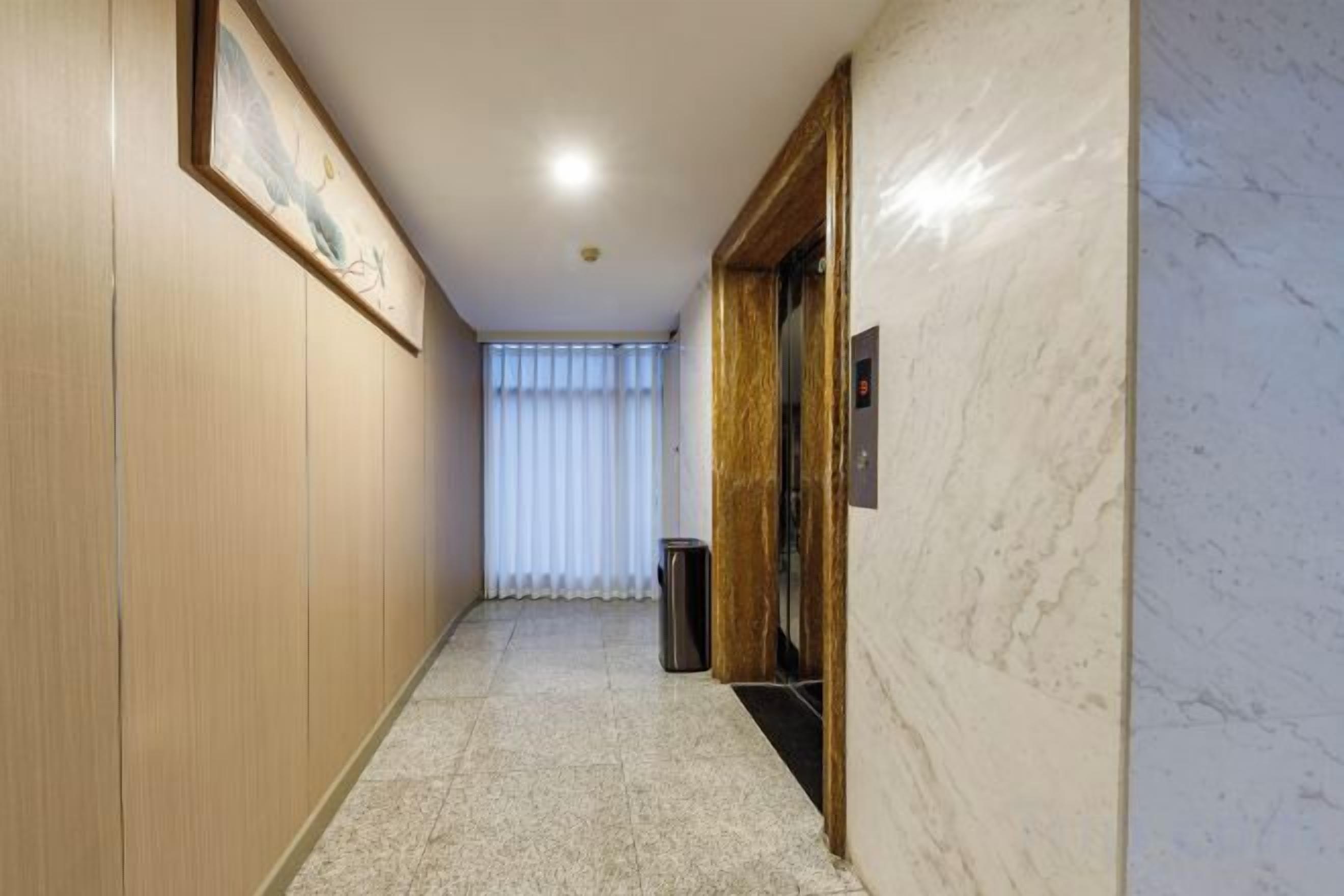 A hallway with a tiled floor, a trash bin, and a door with a handle.
