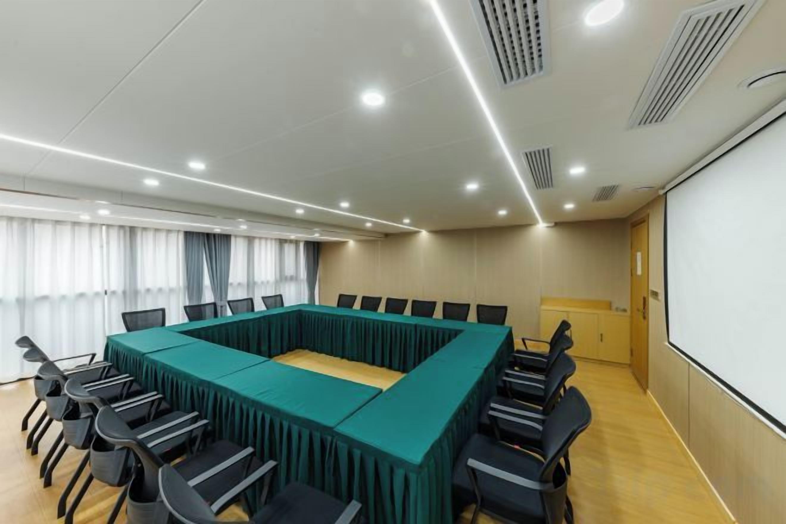 Sala de conferência com uma longa mesa, cadeiras, tela de projetor e janela com cortinas.