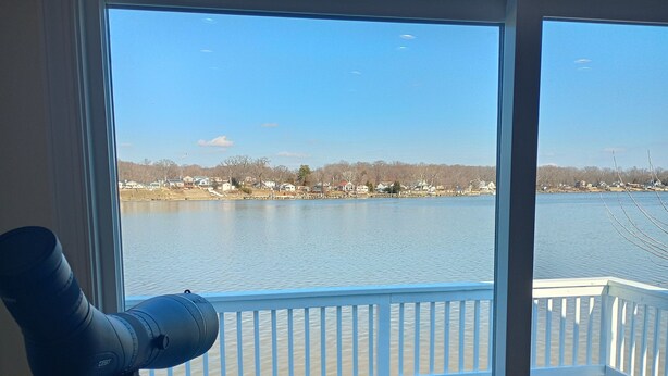 A telescope on a balcony overlooking a lake with houses in the background. - Serene 3-bedroom waterfront newly renovated house, AC, Fast WiFi, Patio (White Marsh)