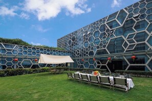 An outdoor area with a table set up for dining, a tent, and a building with a geometric facade. - Sunflower Hotel & Residence Serviced apartment (Shenzhen)