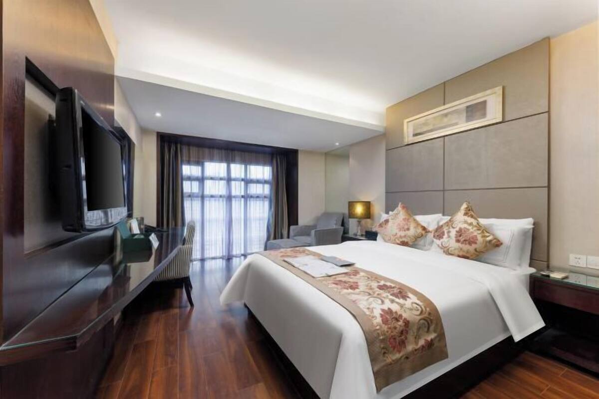 A hotel room with a bed, a TV, a desk, and a window.