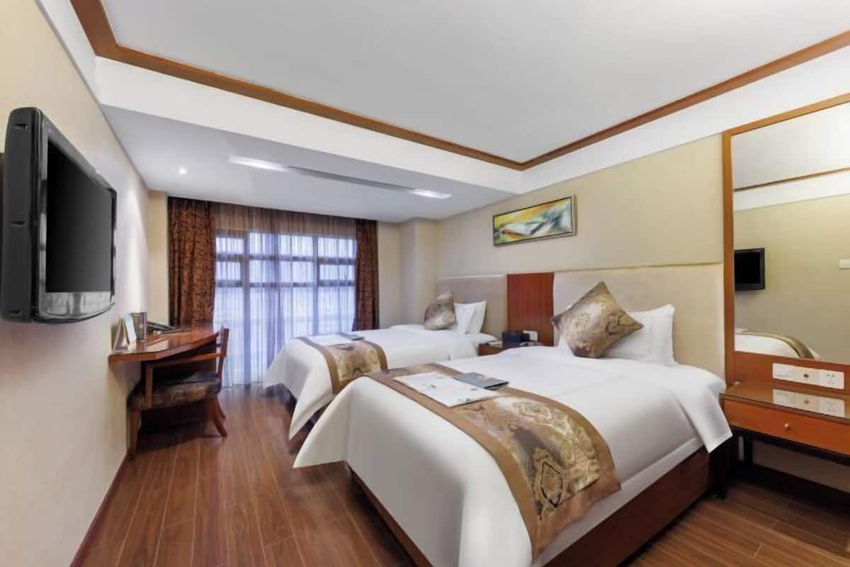 A hotel room with two beds, a TV, a desk, and a large mirror.
