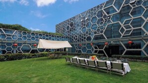 An outdoor dining area with a hexagonal glass facade building, tables, chairs, and a white canopy. - Sunflower Hotel & Residence Serviced apartment (Shenzhen)