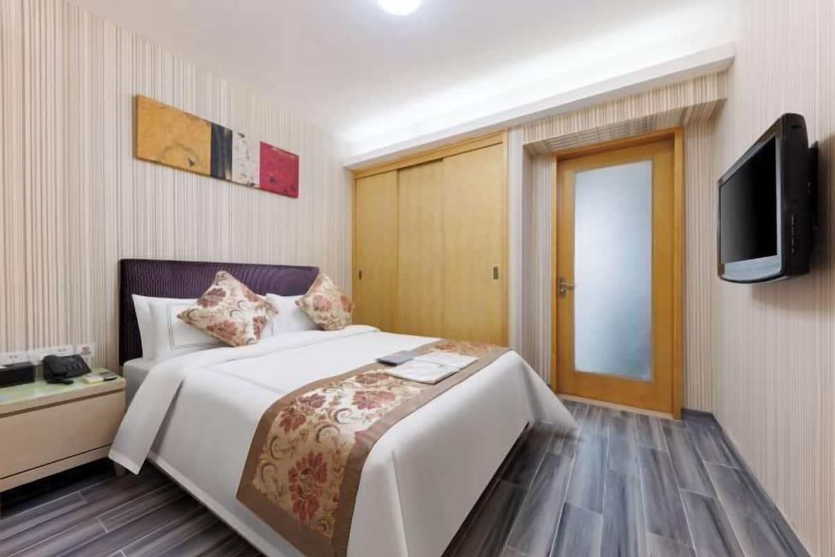 A hotel room with a bed, a nightstand, a television, and a wardrobe.