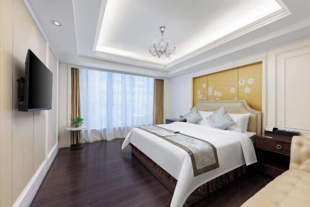A hotel room with a large bed, a television, a chandelier, and a window with curtains.