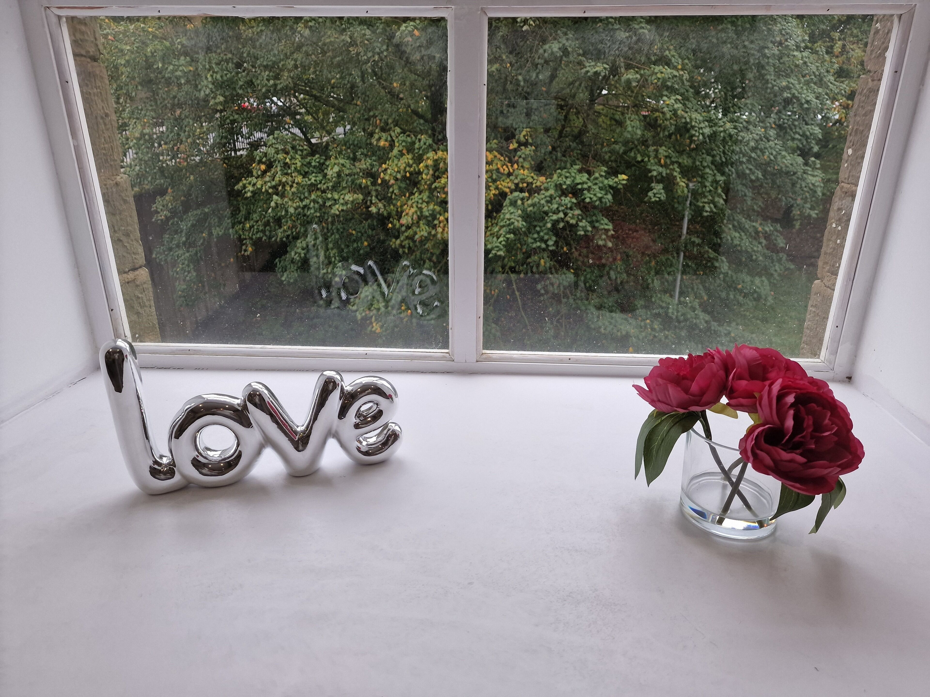 A window with a decorative 'LOVE' sign and a vase with a single red flower.