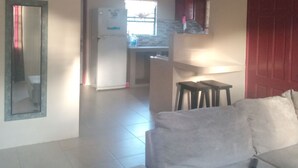 A living room with a sofa, a dining area with a table and chairs, a kitchen in the background, and a red door. - Room-near air and Ferry Ports, Shops & b (Castries)