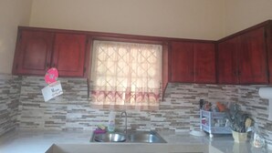A kitchen with a sink, a window with a patterned curtain, and wooden cabinets. - Room-near air and Ferry Ports, Shops & b (Castries)