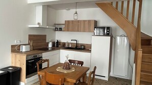 A compact kitchen with wooden cabinets, a dining table, and a staircase. - Cayeux sur Mer. Family home 2 steps from the sea! (Cayeux-sur-Mer)