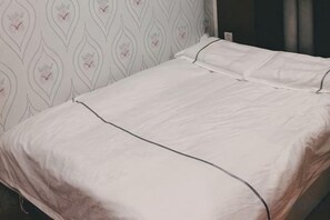 A bed with a white bedspread and matching pillows, a patterned wall behind it, and a visible power outlet on the wall. - Pebble Motel (Shanghai Gucun Park Jutai Road) (Shanghai)