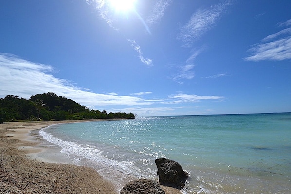 Une plage Ă lâeau claire, un promontoire rocheux et une cĂŽte lointaine bordĂ©e de vĂ©gĂ©tation.