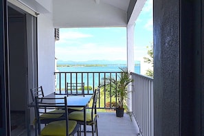 Un balcon avec une table et des chaises, un pot de fleurs et une vue sur la mer et les montagnes.