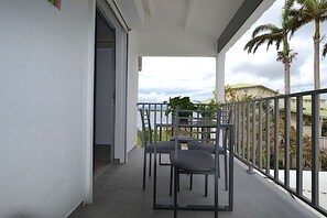 A balcony with chairs, a table, and a view of palm trees and buildings.