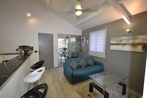 A compact living space with a kitchenette, a sofa, a glass coffee table, and a ceiling fan.