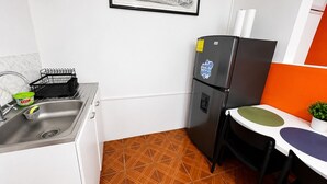 Ett kompakt kök med en diskho, ett svart kylskåp, ett matbord med en stol och ett mönstrat golv.