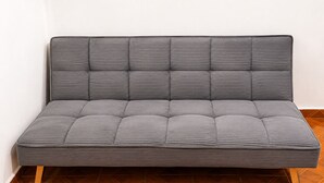 En grå soffa med ett räfflat ryggstöd och sittdynor, placerad på ett trägolv med ett geometriskt mönster av kakelplattor.