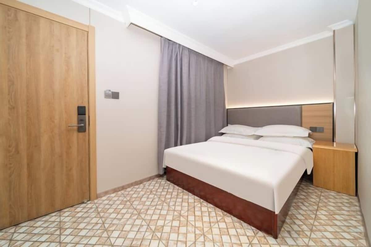Una habitación de hotel con una cama grande, un armario de madera, una mesita de noche y una cortina.