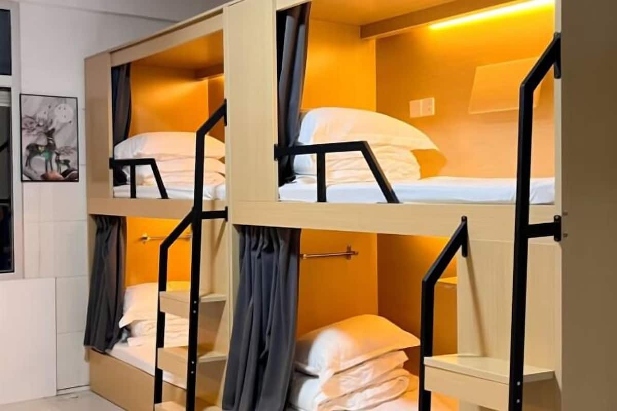 Dormitorio con literas de madera, un escritorio pequeño y una lámpara fijada a la pared.