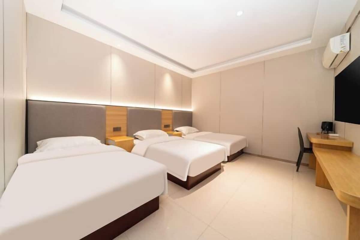 Una habitación de hotel moderna con tres camas, un escritorio de madera y un ventanal grande.