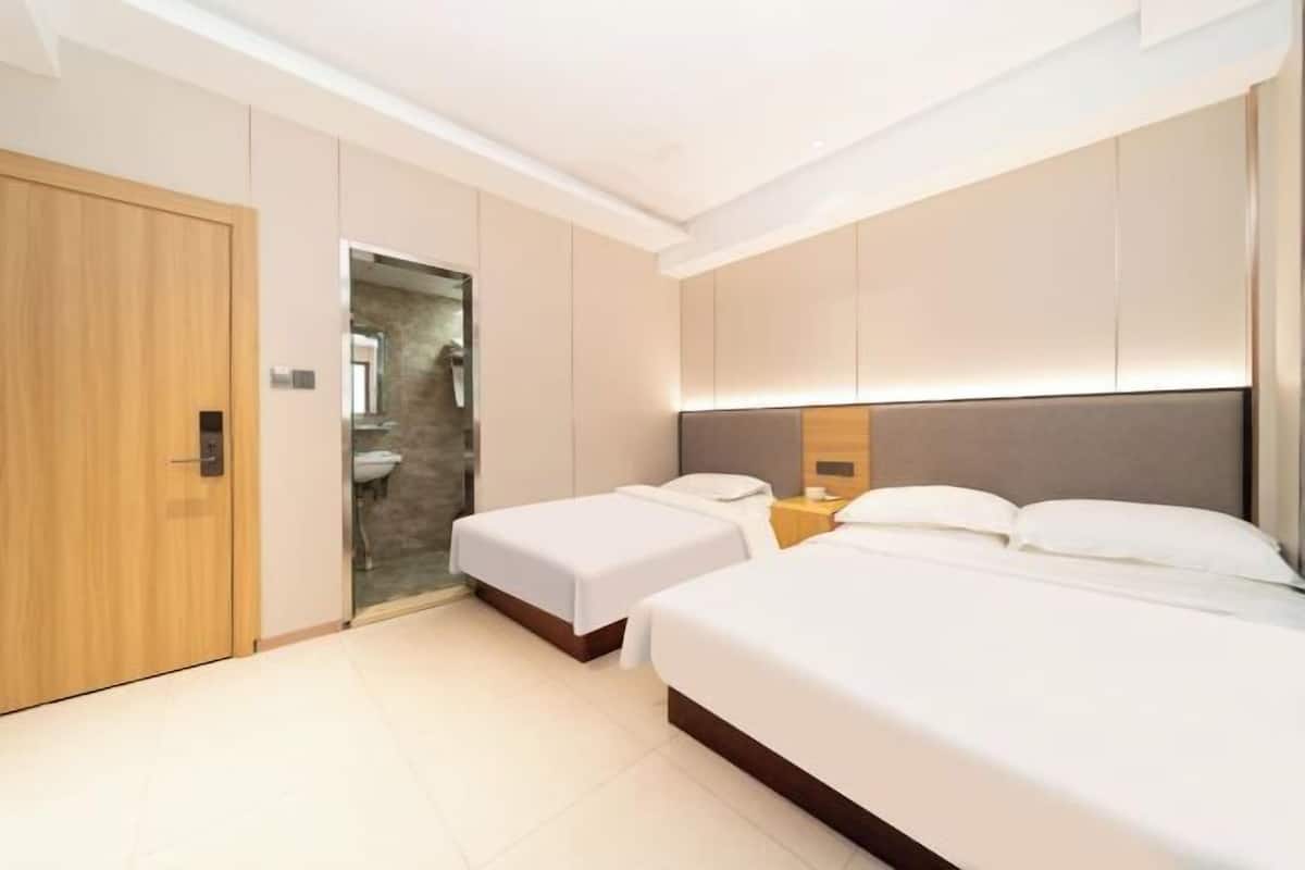 Una habitación de hotel moderna con dos camas individuales, una puerta de madera y un baño visible a través de una puerta abierta.
