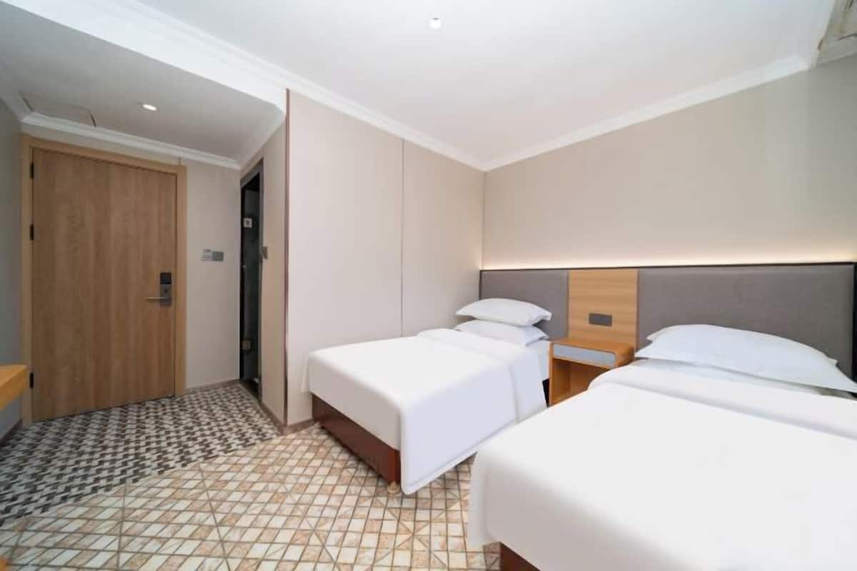 Una habitación de hotel con dos camas, una puerta de madera y piso de baldosas.