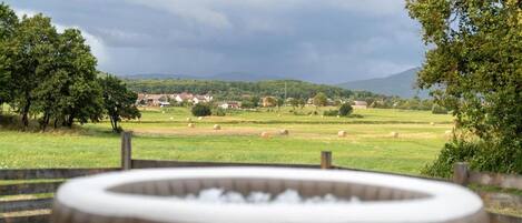 A hot tub in a rural setting with a view of a village and mountains in the distance.