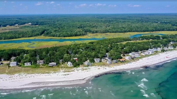 Vista aérea de una zona costera con playa, casas y un paisaje boscoso.