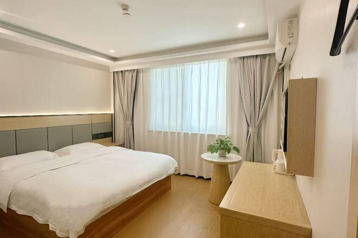 A hotel room with a bed, a round table, a plant, and a mirror.