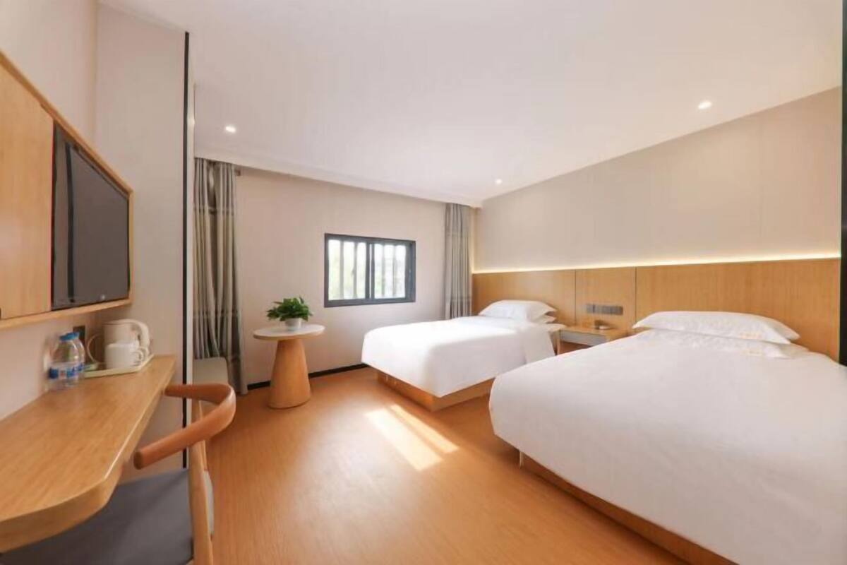 A hotel room with two beds, a desk, a small round table, a TV, and a window with curtains.