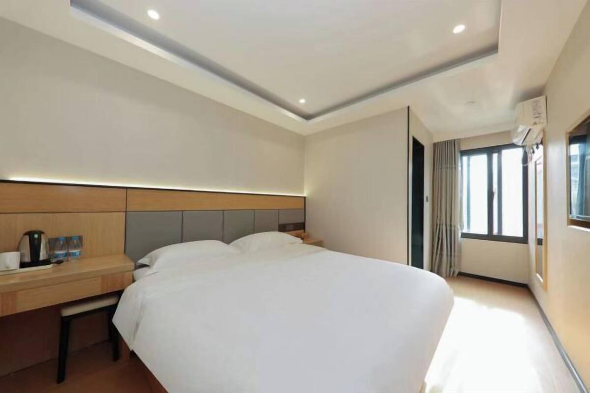 A hotel room with a bed, bedside table, and a window.