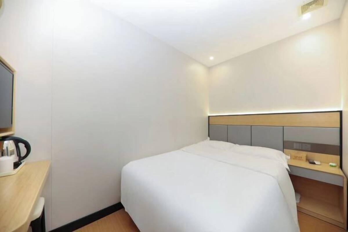 A hotel room with a bed, a desk with a coffee maker, and a small shelf with a mirror and a phone.