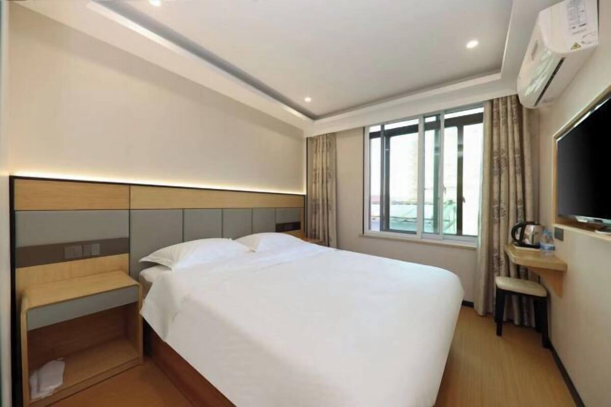 A hotel room with a bed, a nightstand, a TV, and a window with curtains.