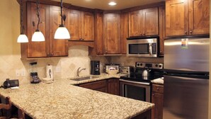 A kitchen with wooden cabinets, granite countertops, a stainless steel refrigerator, a microwave, a stove, and a coffee maker. - Ski-In/Out Luxury 1 Bedroom Condo / Sleeps 4 in Breckenridge at Peak 7 (Breckenridge)