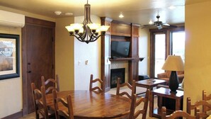 A dining area with a wooden table and chairs, a chandelier, and a television in the background. - Ski-In/Out Luxury 1 Bedroom Condo / Sleeps 4 in Breckenridge at Peak 7 (Breckenridge)