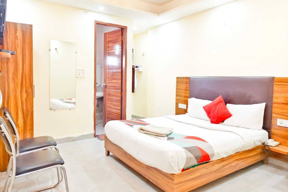 A bedroom with a wooden bed frame, a nightstand, a chair, a mirror, and a door leading to a bathroom.