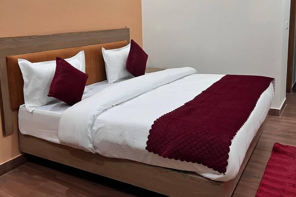 A neatly made bed with white and maroon bedding, a wooden headboard, and a red throw blanket.