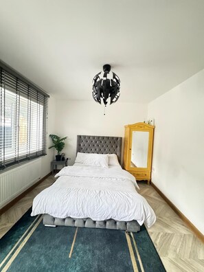 A bedroom with a bed, a large mirror, a potted plant, and a window with blinds. - 1br-sleeps2-parking-nearlondon-central (Erith)