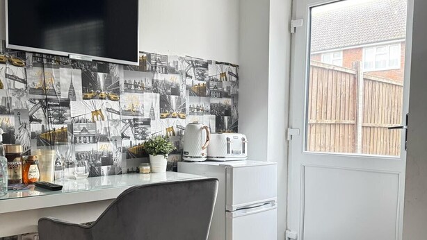 A compact kitchen with a modern design, featuring a flat-screen TV, a refrigerator, and a dining area with a chair. - 1br-sleeps2-parking-nearlondon-central (Erith)