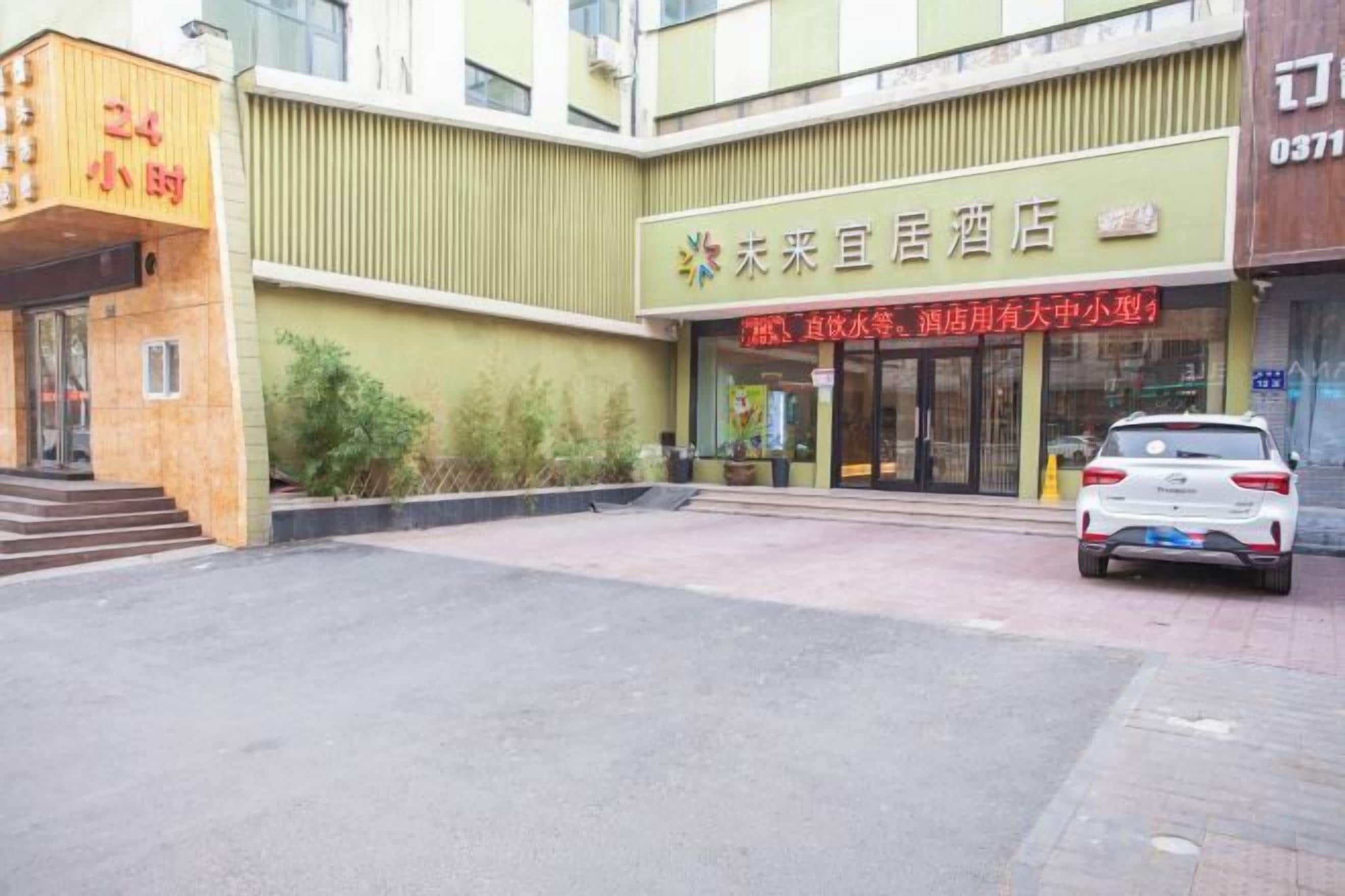 Fachada de hotel verde, un coche estacionado en frente y un letrero con caracteres chinos.
