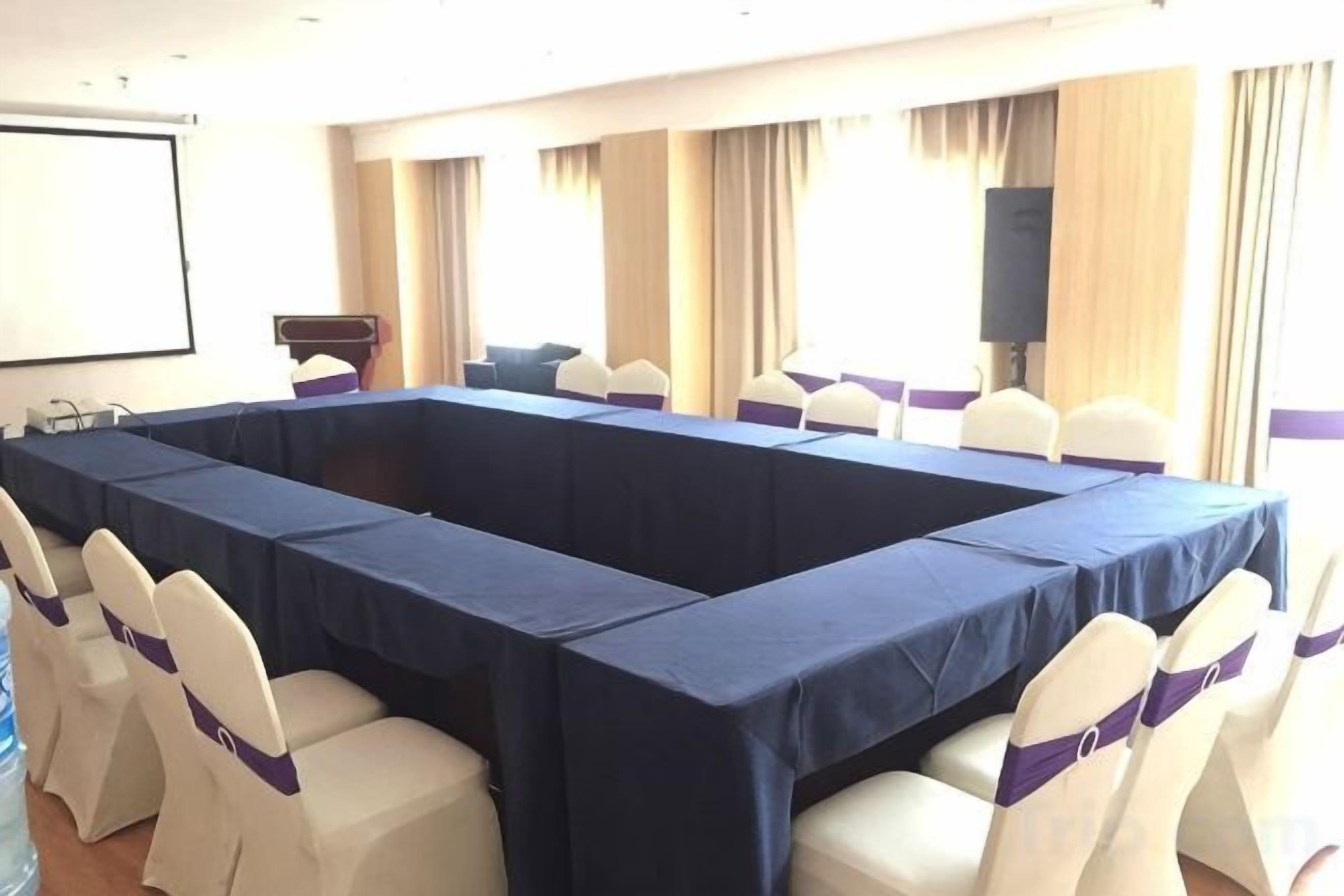 A conference room with a long table, white chairs with purple sashes, and a projector screen.