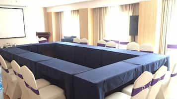 A conference room with a long table, white chairs with purple sashes, and a projector screen.