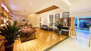 Eine moderne Hotelhalle mit Holzboden, einem Essbereich mit Tisch und Stühlen, einer Rezeption und einer Glastrennwand.