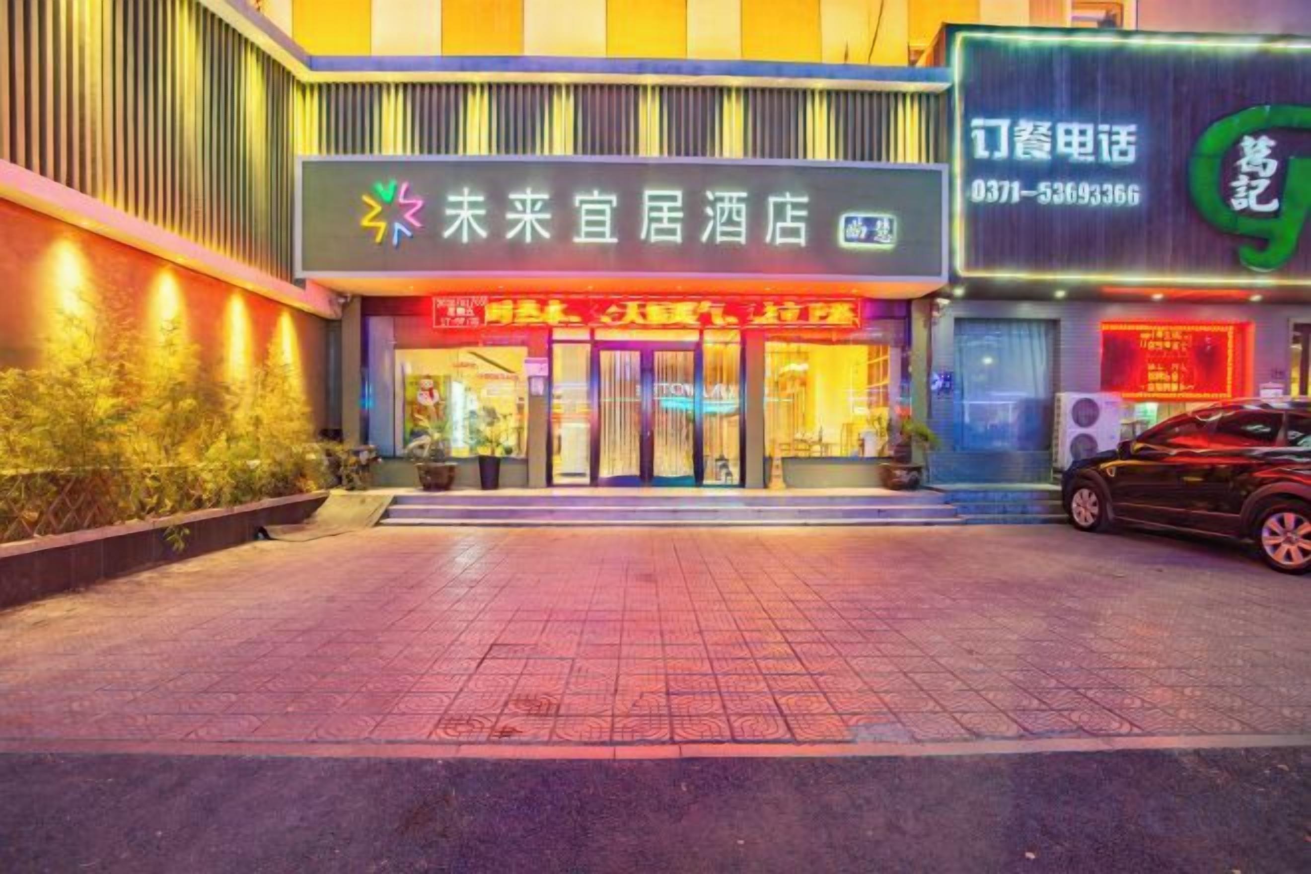 A hotel entrance with a signboard, a reception desk, and a car parked outside.