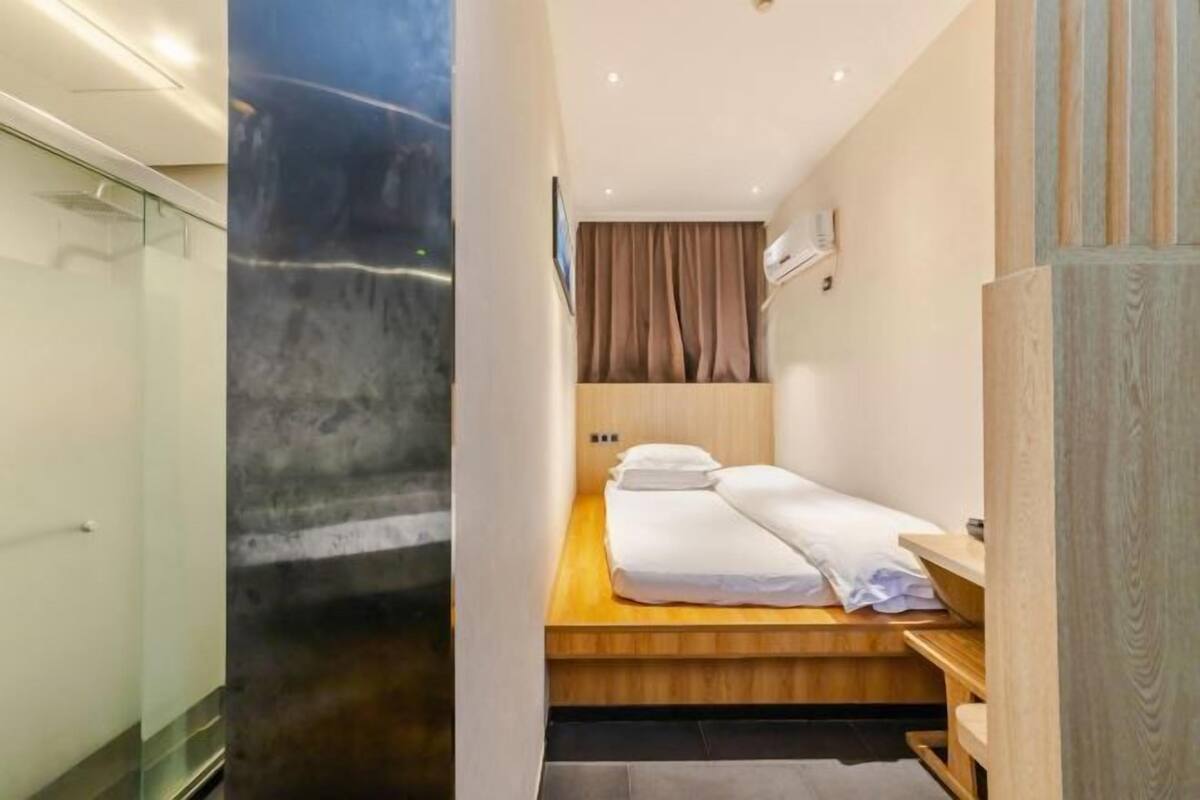 Une chambre d’hôtel avec un lit, un banc en bois, une cabine de douche en verre et une vue sur l’extérieur.